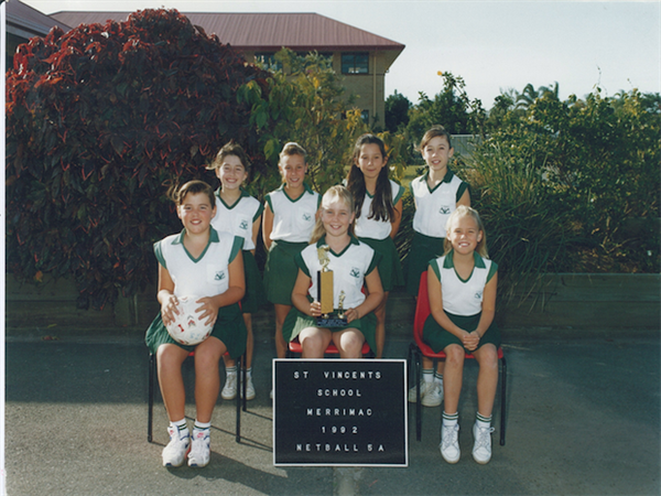 Historical school netball team photo with students in uniform holding a trophy, representing student achievement and school sporting history