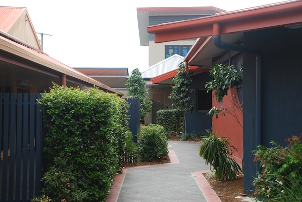 Landscaped school walkway between buildings with gardens and shaded paths connecting learning areas