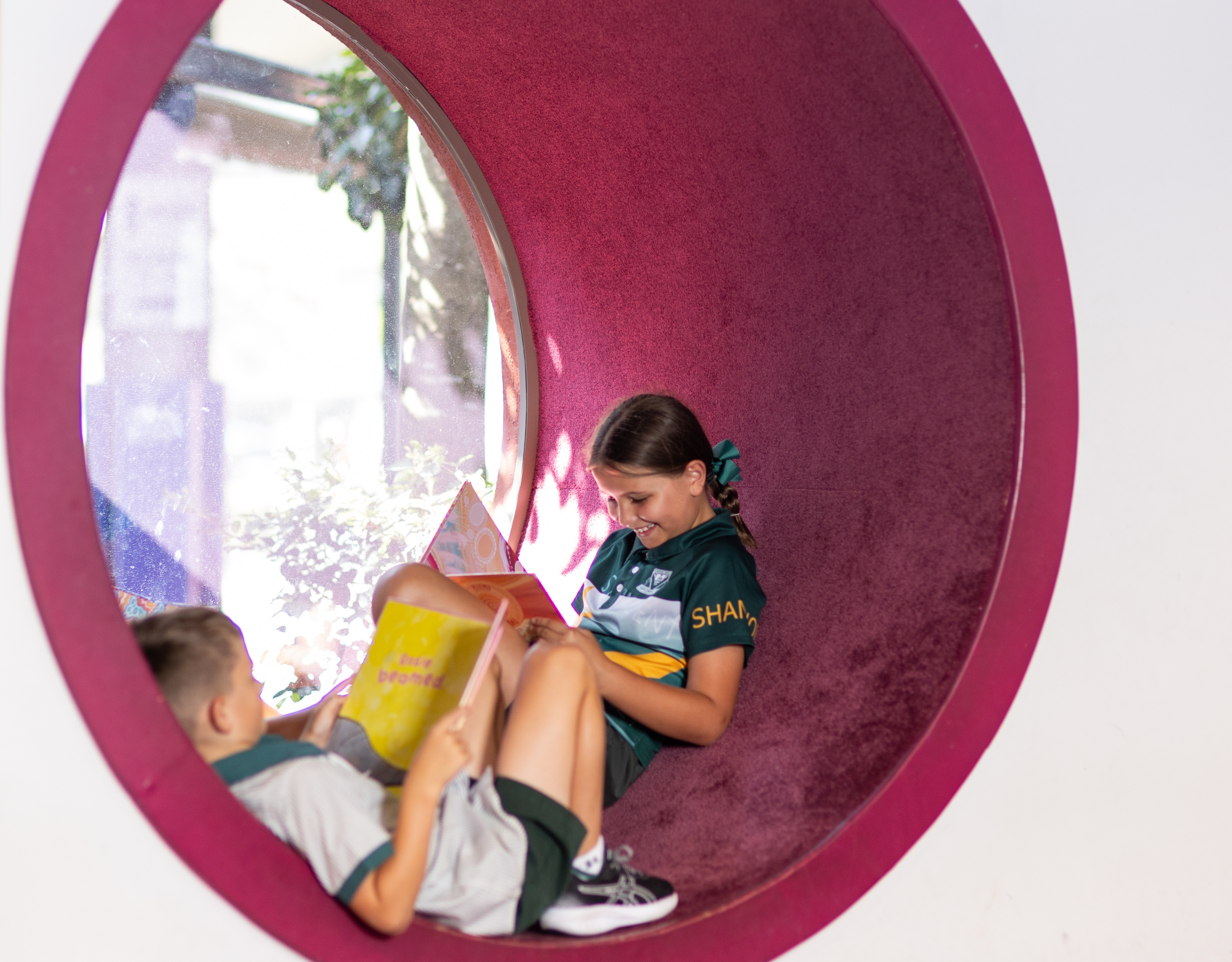 Student reading a book inside a circular reading nook with another student nearby, creating a quiet and engaging learning space