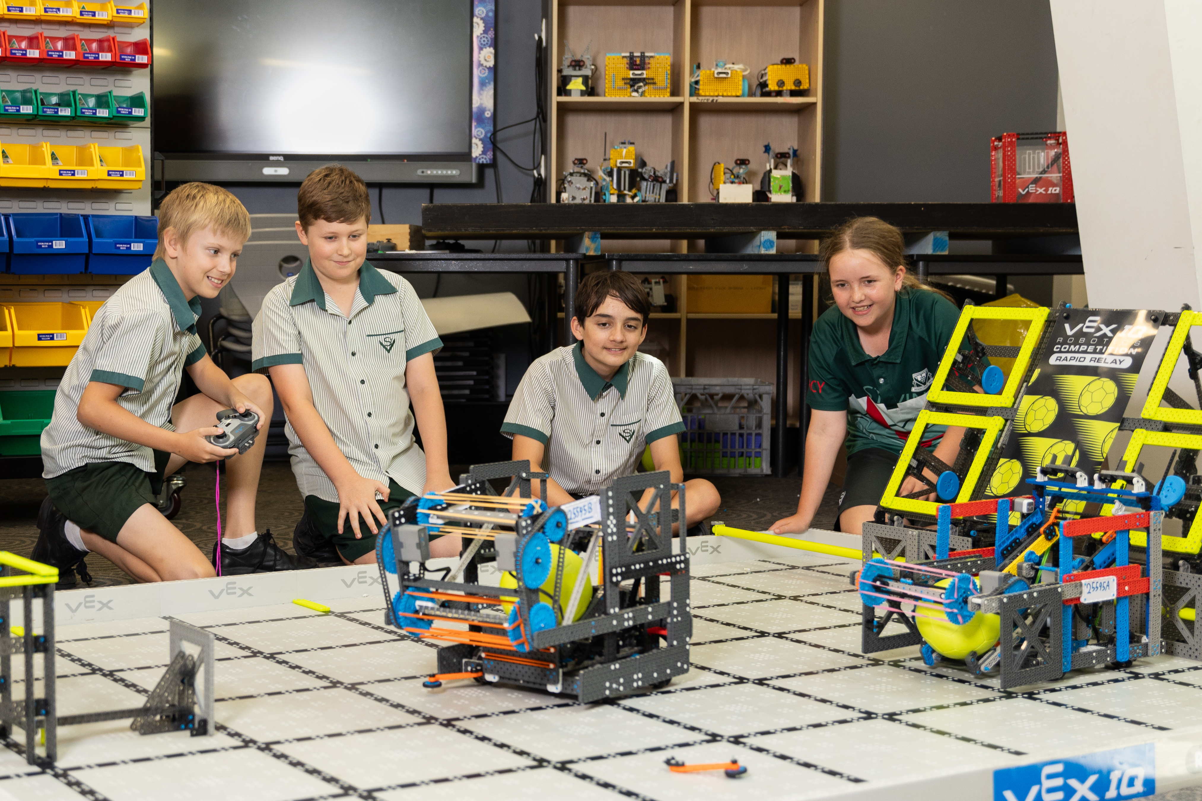Students operating VEX robots on a competition table while collaborating in a classroom robotics activity