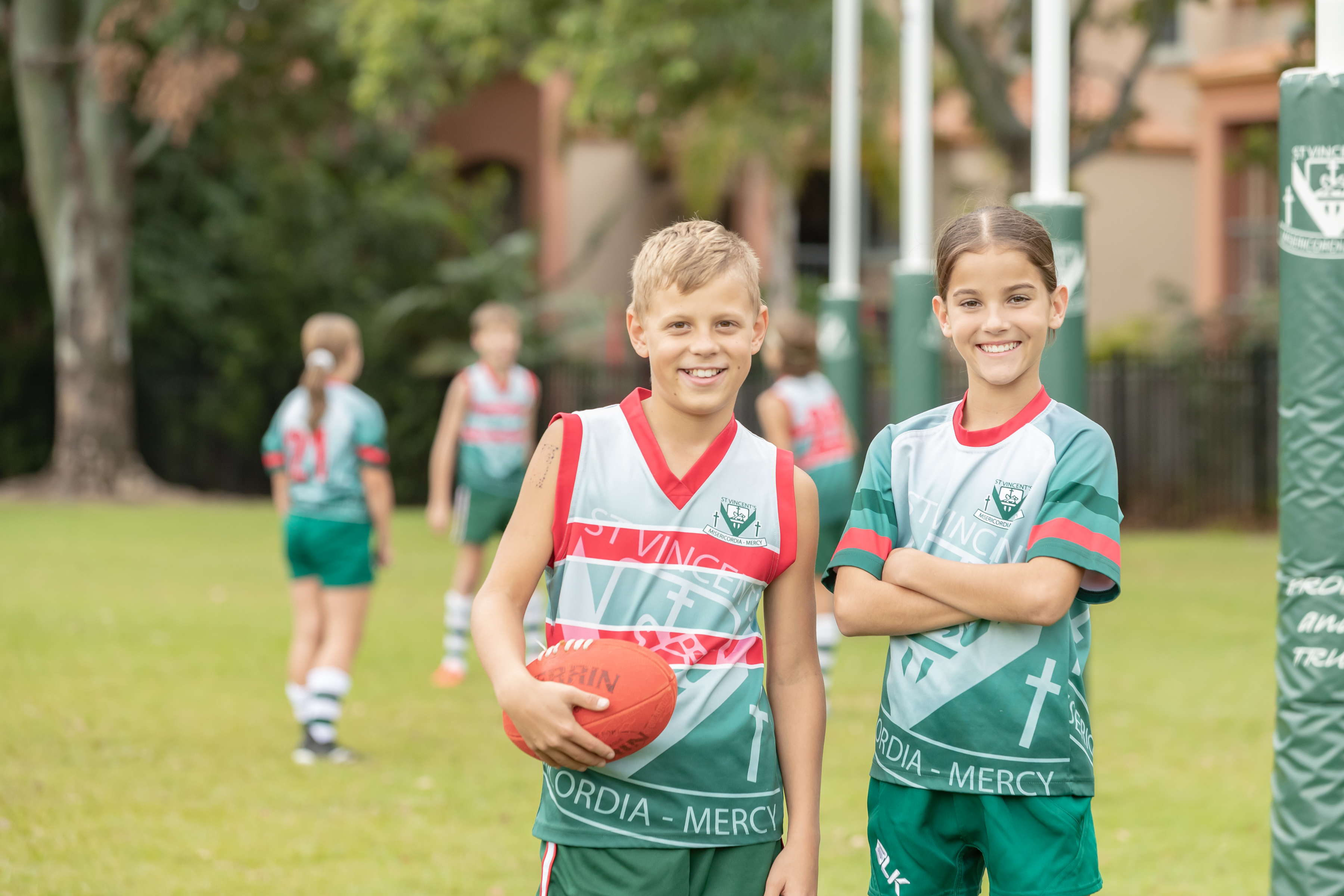 Students standing with a football on a school field while other students play in the background