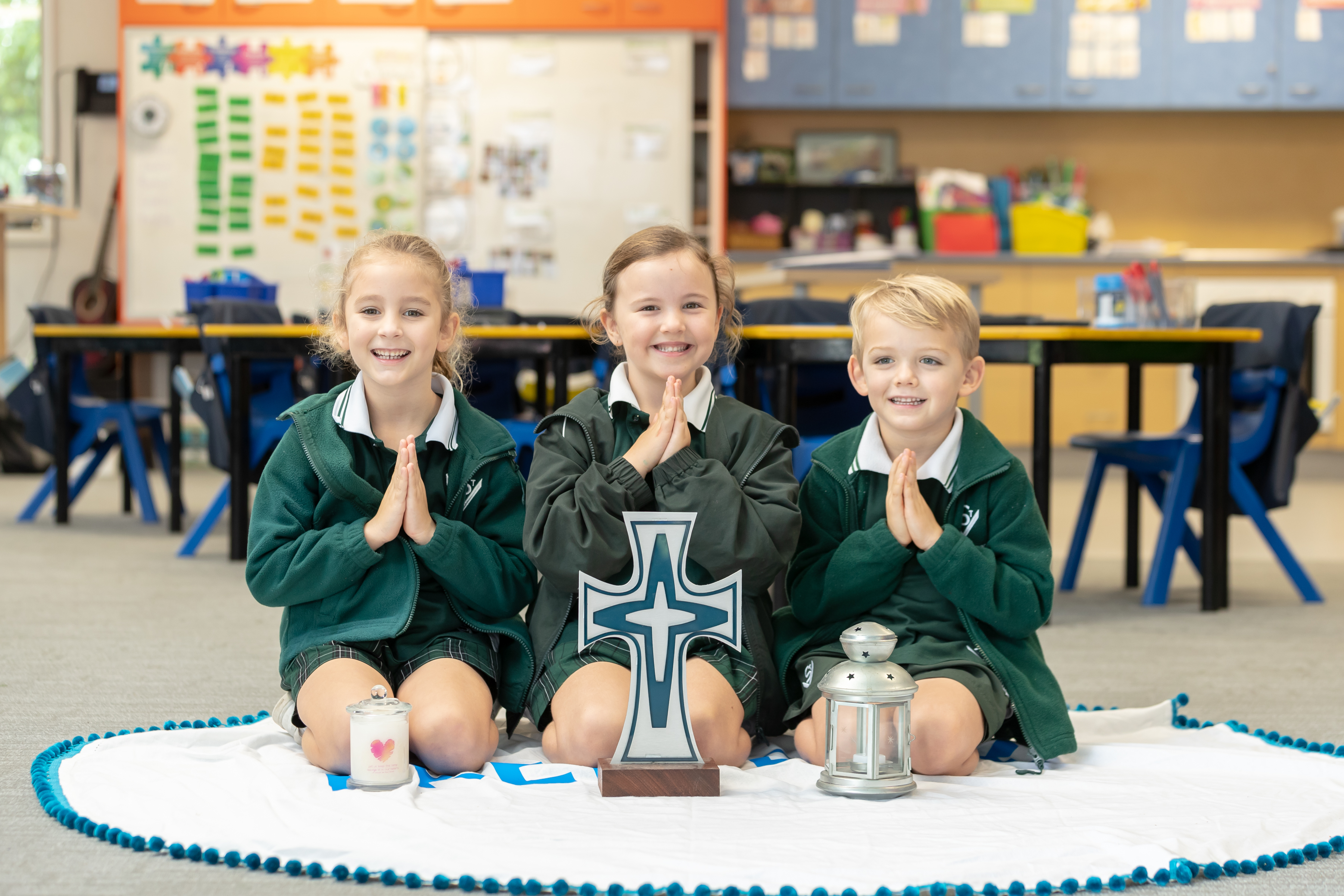 Students in a classroom sitting in prayer with hands together around a cross and lit candles during a Catholic prayer activity