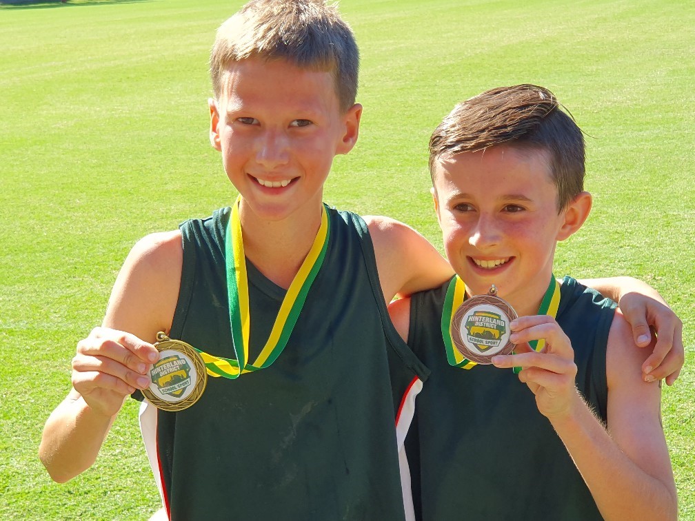 Two students standing together on a sports field holding medals and posing after a school sporting achievement