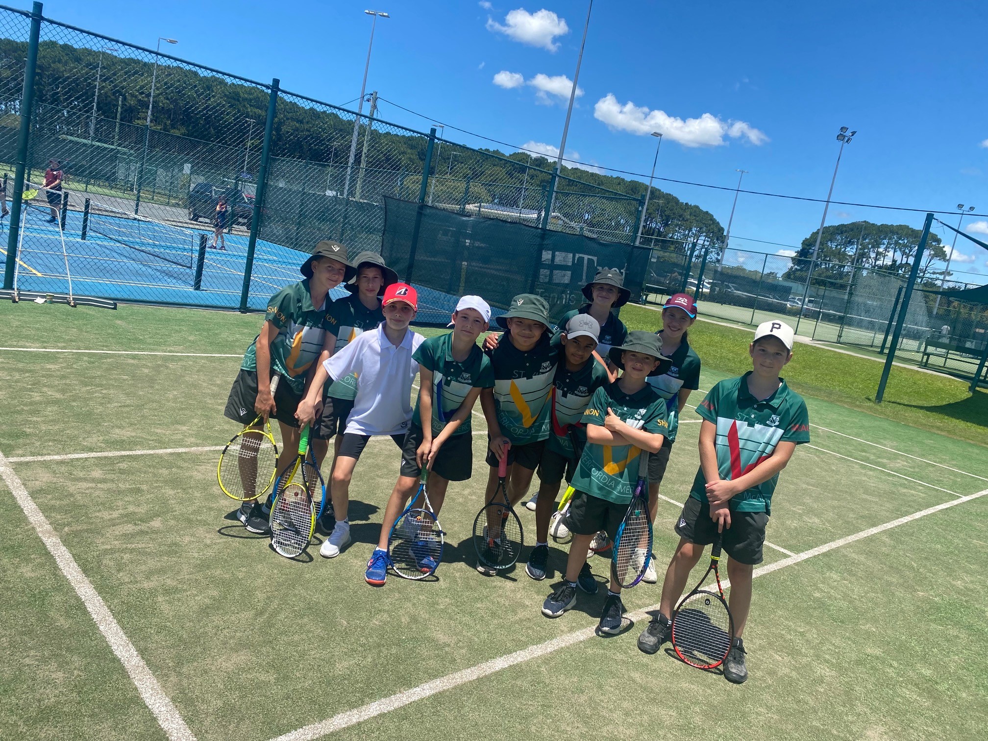 Students standing together on a tennis court holding racquets during a school sports activity
