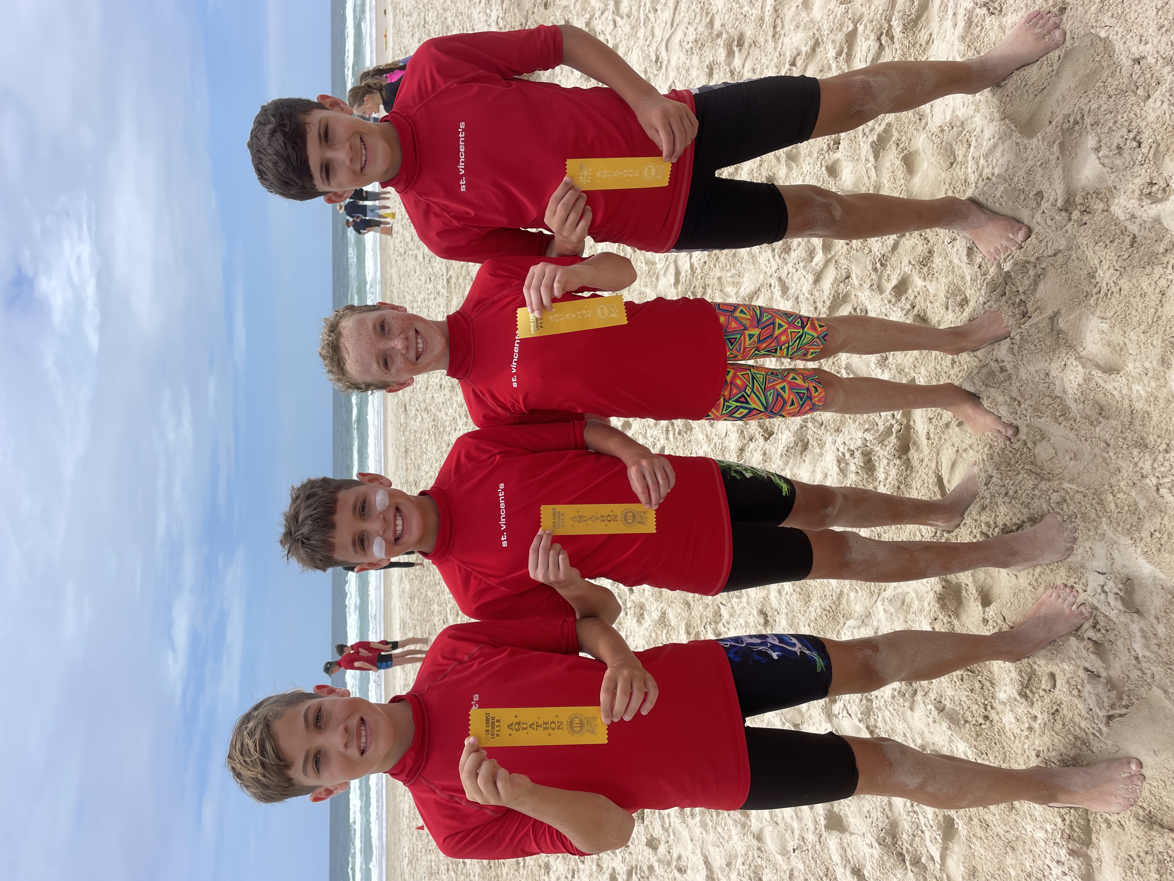 Students standing on a beach holding ribbons during a surf lifesaving or beach sports event