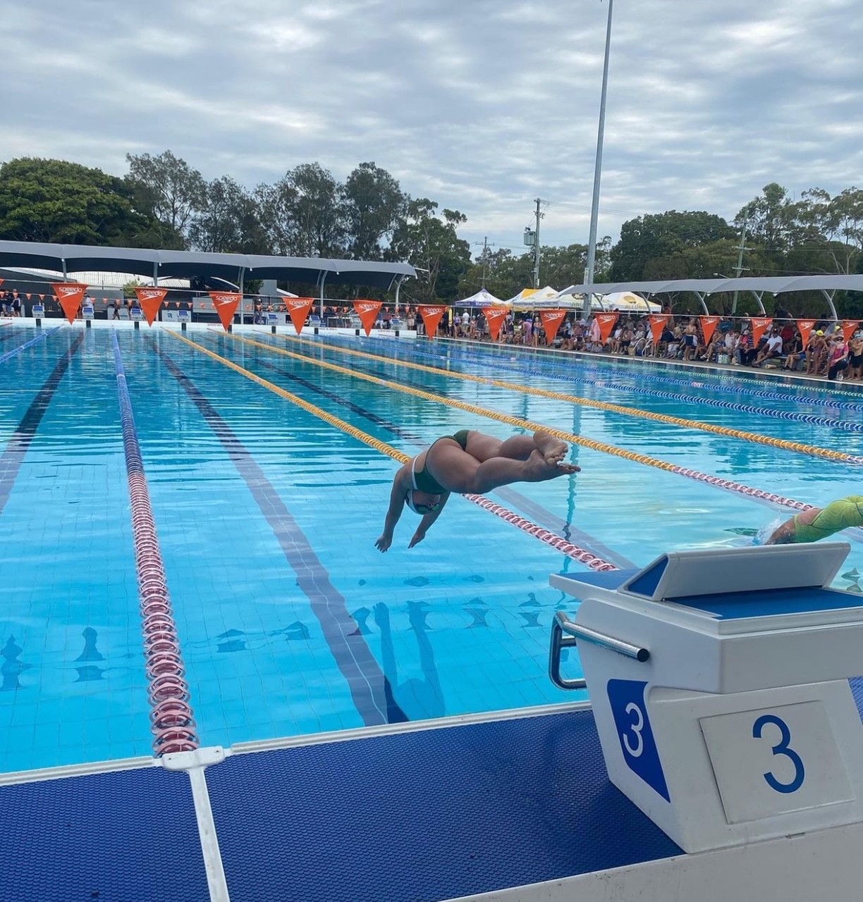 Students competing in a swimming race, diving into lanes in an outdoor pool